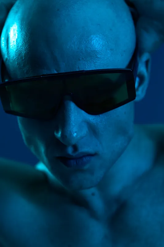 Intense man in sunglasses, showcasing a modern aesthetic, with bold blue light creating a mesmerizing atmosphere and emphasizing his striking features.