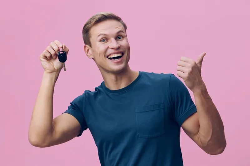 smiling young caucasian man hold car keys show thumb up wear casual blue tshirt isolated on pink background digital nomad happiness concept