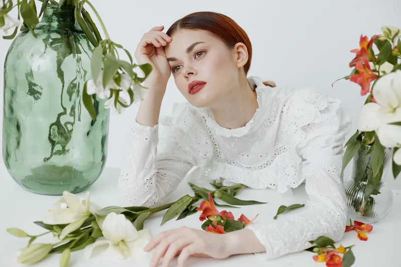 Elegant woman in white lace blouse resting among fresh flowers in a serene environment, evoking emotions of tranquility and beauty