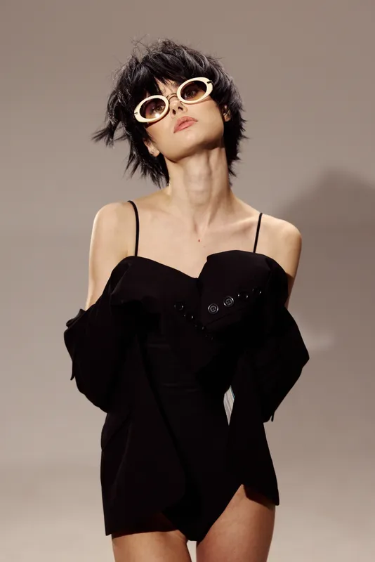 Stylish woman in black dress wearing white sunglasses posing confidently with modern hairstyle.