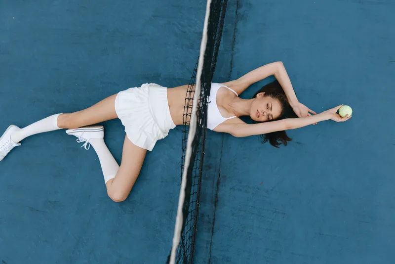 Young female tennis player resting on a blue court, wearing a sporty outfit, embodying relaxation and focus after a match, showcasing athleticism and summer vibes