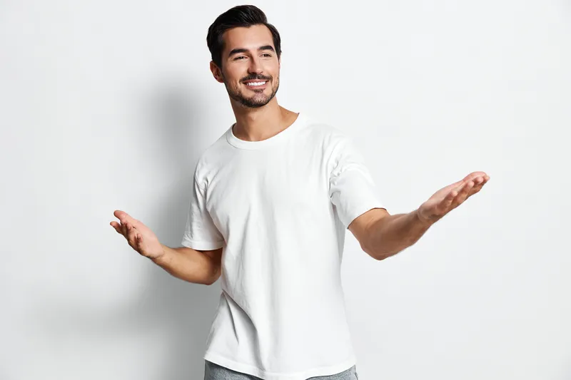 Smiling man wearing a white t-shirt, looking at the camera with arms outstretched, showcasing a friendly demeanor isolated on plain solid white background. Lifestyle concept.