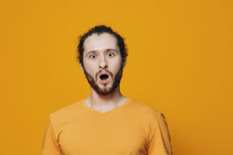 Surprised young man with a beard expressing shock against a vibrant yellow background, highlighting emotions and modern style in portrait photography