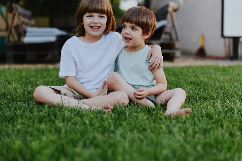 Happy children sitting on green grass, enjoying a sunny day outdoors, showcasing the innocence and joy of childhood in a vibrant setting.