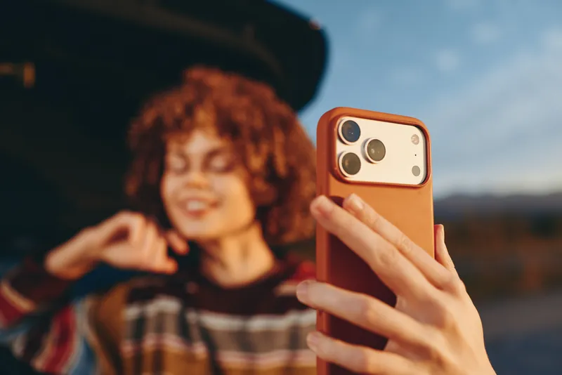 woman lifestyle outdoors, hand holding smartphone phone for selfie, curly haired woman smiling, portrait view at sunset, casual street style, shallow depth of field, natural light