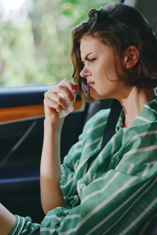 A young woman sits in a car, deep in thought, wearing a green striped shirt, captured in soft natural light.