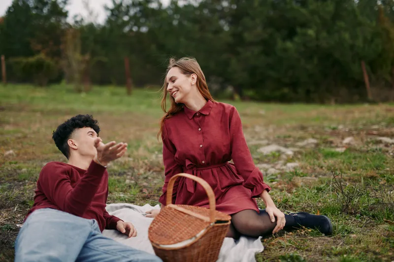 Young couple enjoying a candid picnic on a grassy field, sharing a genuine laugh and relaxed conversation, natural poses and warm tones convey authenticity and real connection.