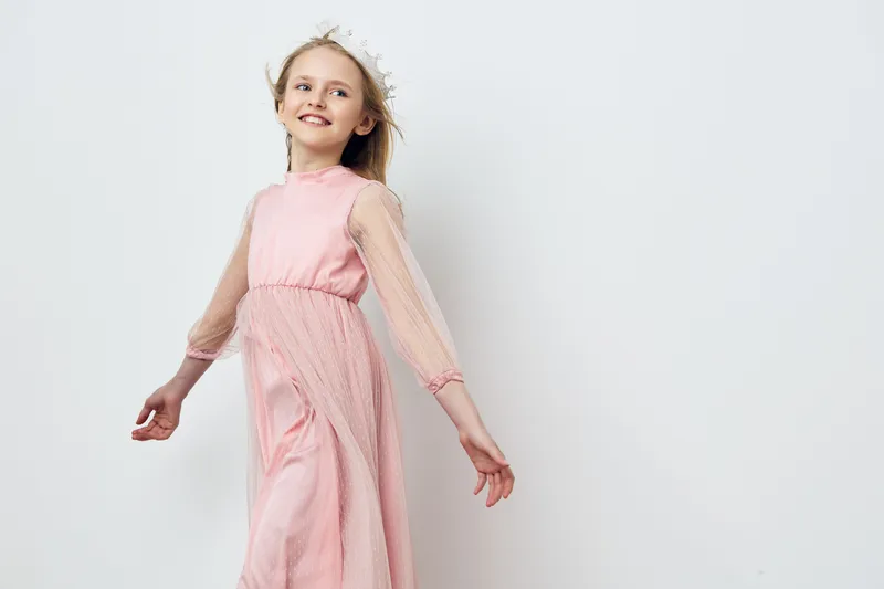 A joyful young girl in a pink dress twirling with happiness against a simple white background, embodying a playful and carefree childhood spirit