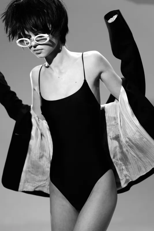 Black and white portrait of a woman in sunglasses and black bodysuit with coat, fashionable and stylish look.