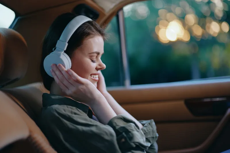 Young woman enjoying music in car with headphones, conveying happiness and relaxation in a warm evening setting, ideal for lifestyle and wellness themes.
