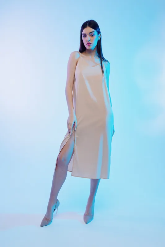 Elegant woman in a beige dress poses confidently against a blue background. The fashion image highlights beauty, style, and modern trends in clothing and footwear.