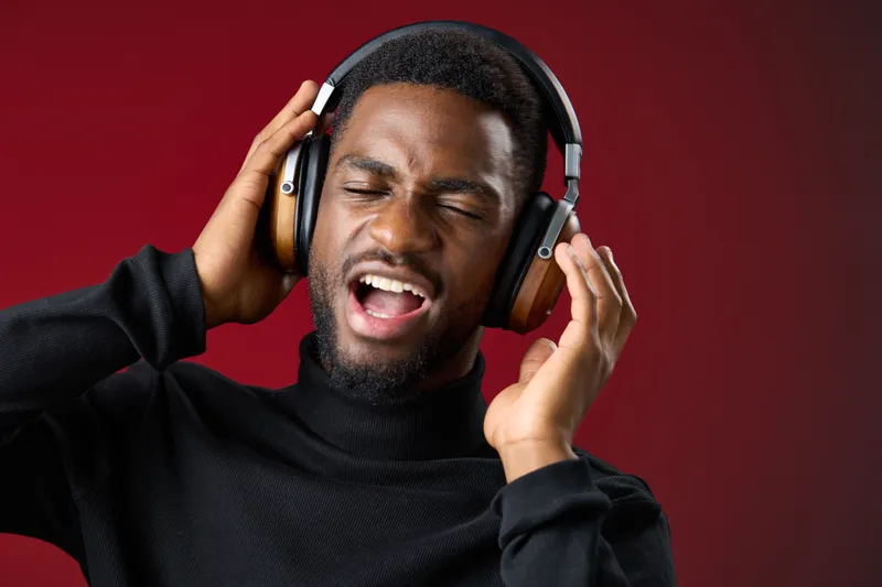 Young black man enjoying music with headphones, expressing happiness, in a warm toned backdrop Emphasizes joy, music, and modern lifestyle