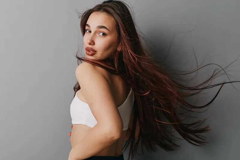 Woman with long hair turning back and looking at camera with confident expression against gray background. Beauty, fashion, portrait, hairstyle, casual style, studio shot.
