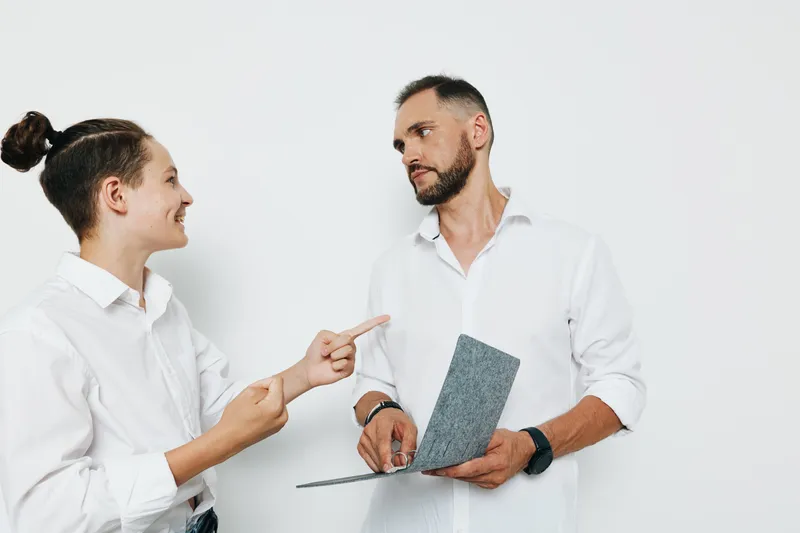 A professional man in a white shirt stands against an isolated colored background, exuding confidence and focus as he discusses work, showing calm determination and engaged curiosity.