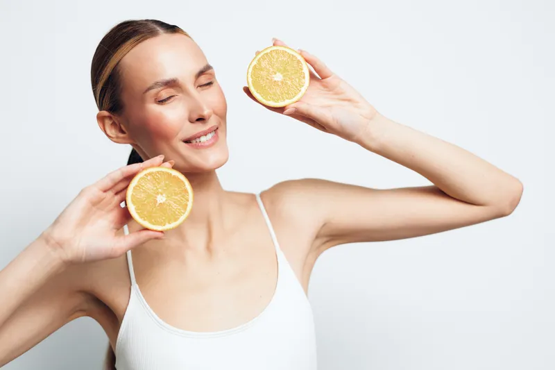 Woman holding lemon slices, smiling with fresh skincare routine, beauty and spa concept, citrus treatment on light background, clean copy space for advertising