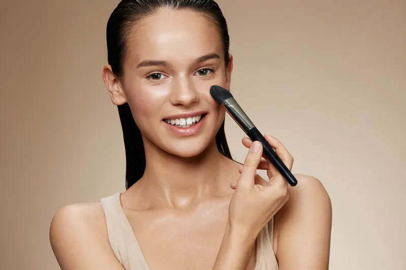 Portrait of a young woman applying makeup with a brush, showcasing natural beauty and confidence, ideal for beauty and cosmetics concepts