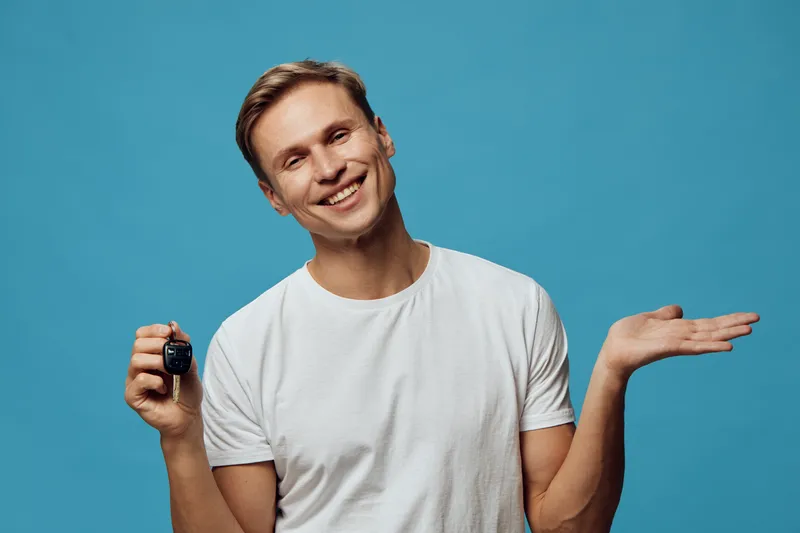 Smiling man holding car key gesture friendly confident casual clothing isolated on blue studio background portrait. People lifestyle concept