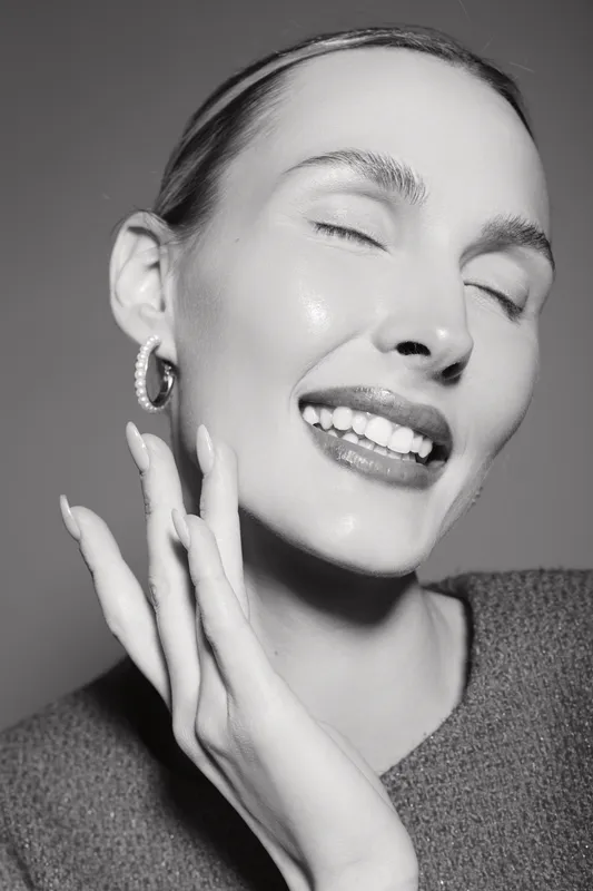 Happy white woman with light skin smiling with closed eyes and hand near face in studio. Concept of joy, beauty, and natural expression.