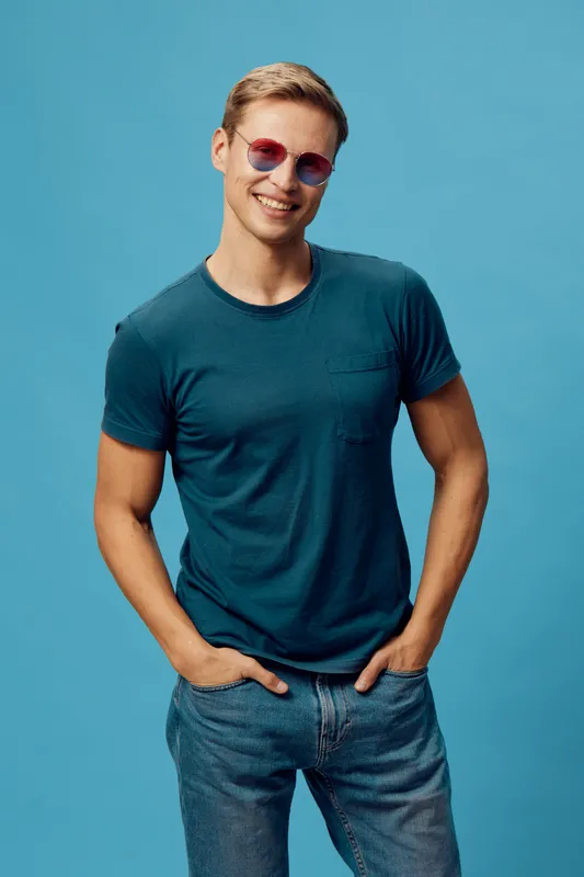 smiling man in sunglasses casual t-shirt blue background confident standing hands in pockets freelance on stock photo