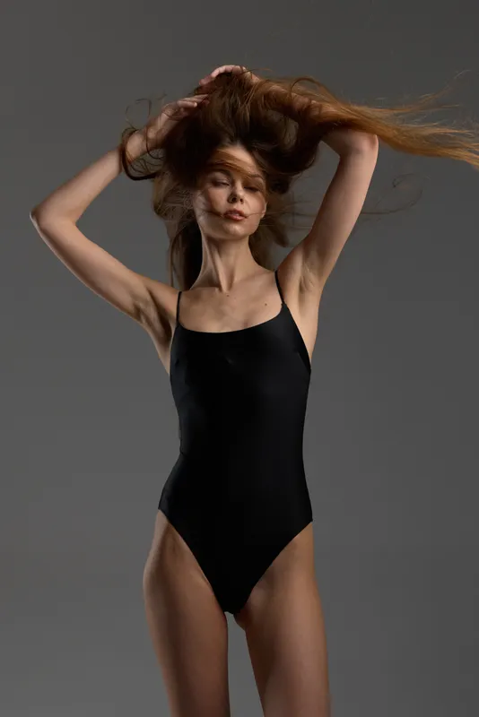 slender woman in black bodysuit with flowing hair standing against dark background