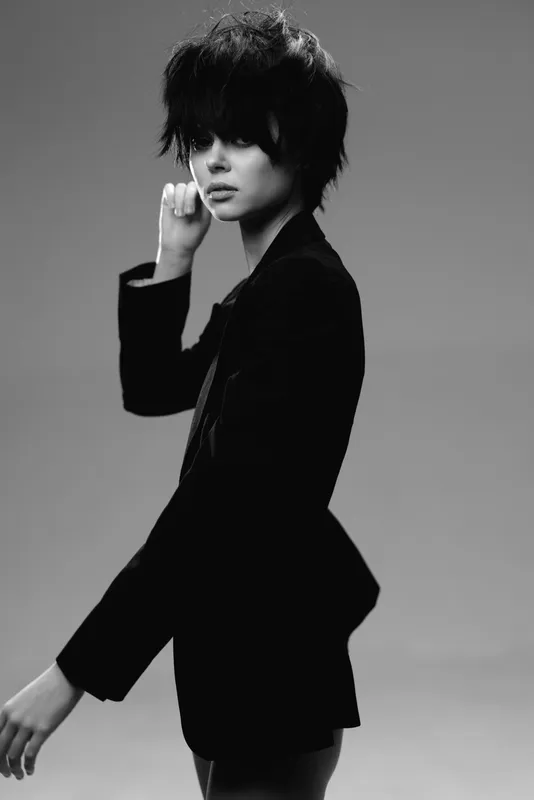 Black and white portrait of a young woman with short hair wearing a dark blazer, showing a serious and thoughtful expression.