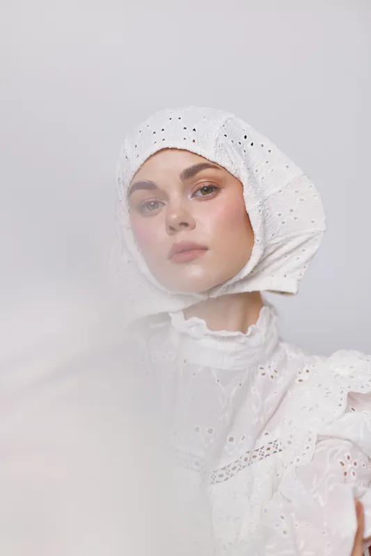 Ethereal young woman in a white headscarf and dress, conveying tranquility and elegance against a soft white background Perfect for fashion and beauty concepts