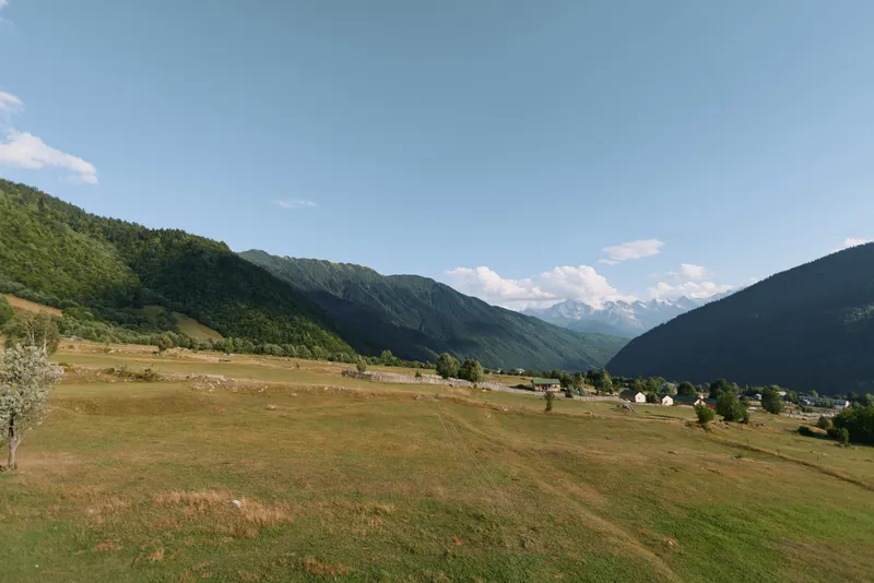 A wide open meadow nestled between rolling hills and distant mountains under a clear blue sky, conveying peaceful rural scenery suitable for nature, travel, and outdoor projects.