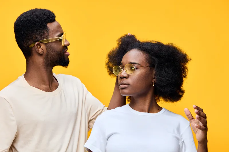 Young African couple with stylish glasses against a bright yellow background, showcasing confidence and beauty in a modern lifestyle setting