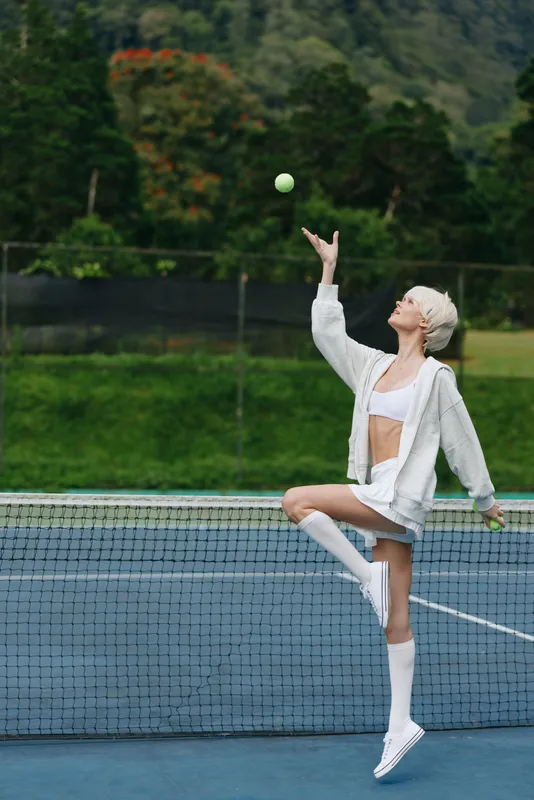 Stylish female tennis player serving on the court in athletic wear, showcasing confidence and determination against a vibrant natural backdrop