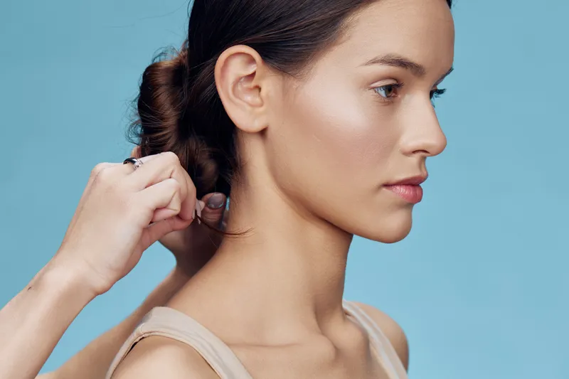 Portrait of a serene young woman with a bun hairstyle, captured against a soft blue background, reflecting elegance, beauty, and a sense of calm