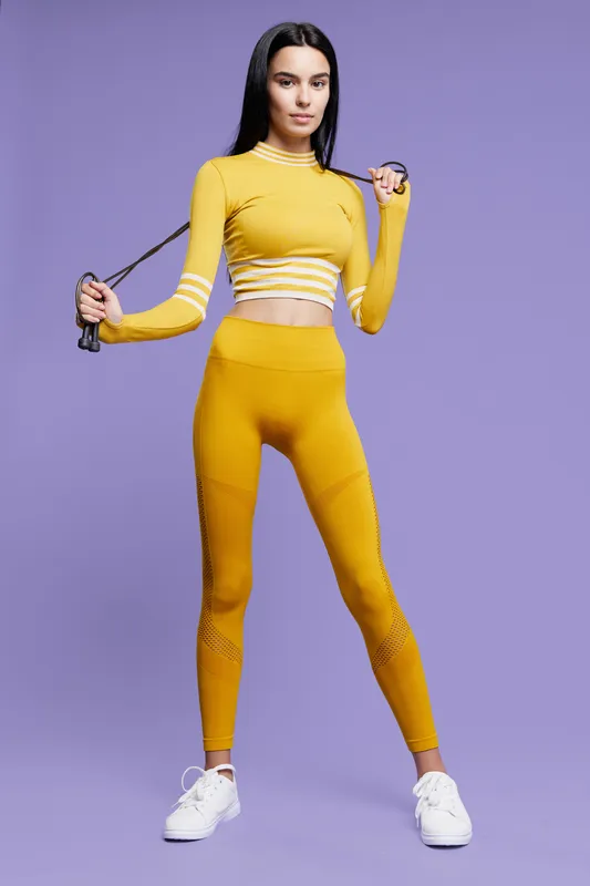 woman sport fitness wearing yellow activewear, holding jump rope, standing on purple background, athletic young female in workout clothing