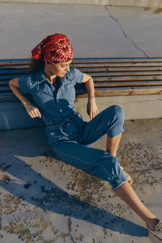 Lifestyle woman in modern boho-western denim street style with red bandana sitting outdoors in warm film color sunlight, relaxed pose, casual summer fashion.