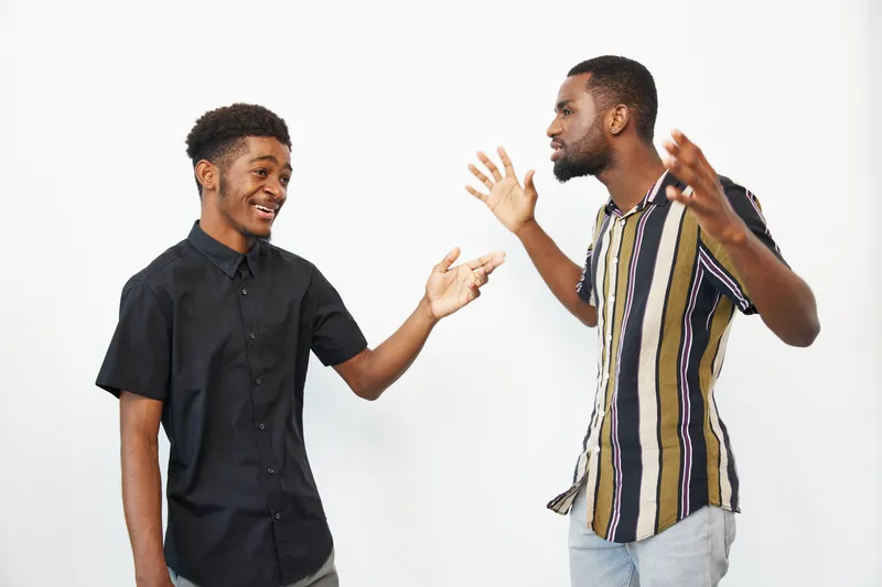 Engaging black man expressing emotions while talking with a friend, showcasing enthusiasm and connection in a bright, minimalistic setting.