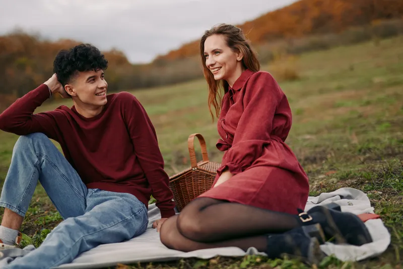 A candid moment between two friends outdoors on a calm autumn day, capturing authenticity and genuine connection on a rustic park blanket.