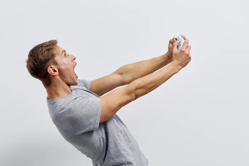 excited young caucasian man hold joystick play video game grey t-shirt isolated on white background digital entertainment concept