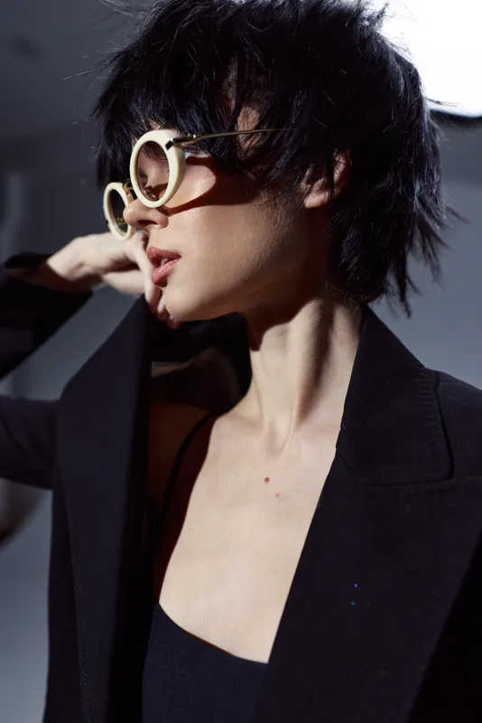 Stylish woman with short dark hair wearing large sunglasses and black clothing in dramatic light