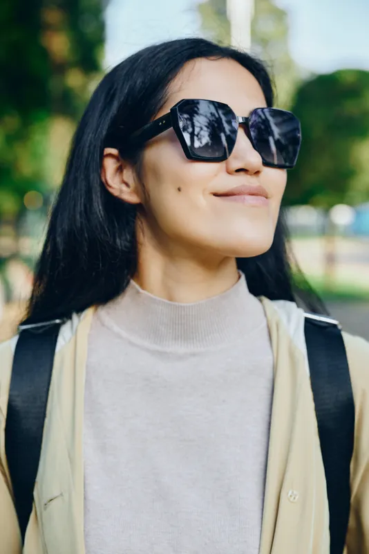 Sunglasses wearing woman in an outdoor park, stylish casual outfit, sunny day, relaxed smile, capturing a fashion and lifestyle moment suitable for streetwear, travel and leisure visuals