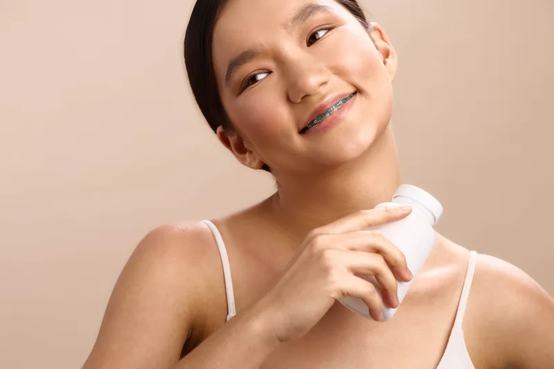 asian woman smiles while applying a skincare product in a bright studio, exuding confidence, joy, and wellness in a clean, modern setting that communicates healthy beauty and daily care.