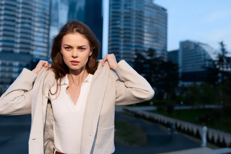 Confident woman in business attire adjusting her jacket against a modern city skyline, exuding professionalism and determination.