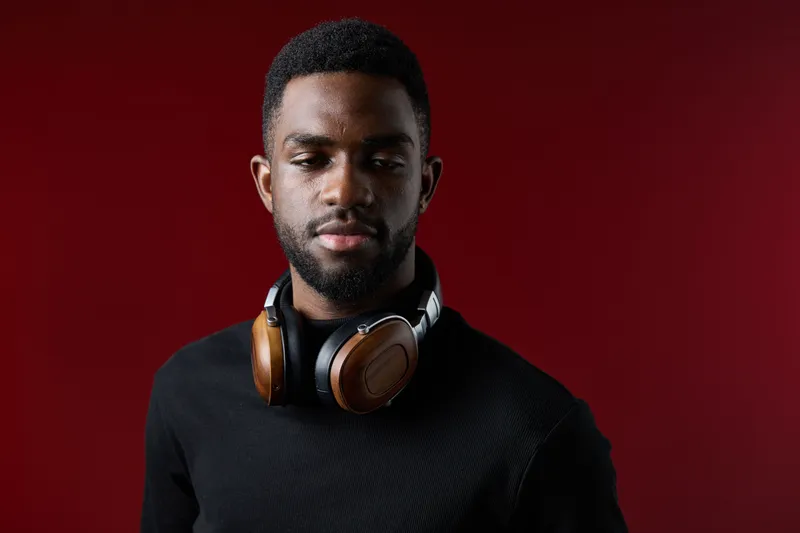 Young Black man with headphones on a red background, showcasing confidence and style, perfect for music and lifestyle concepts