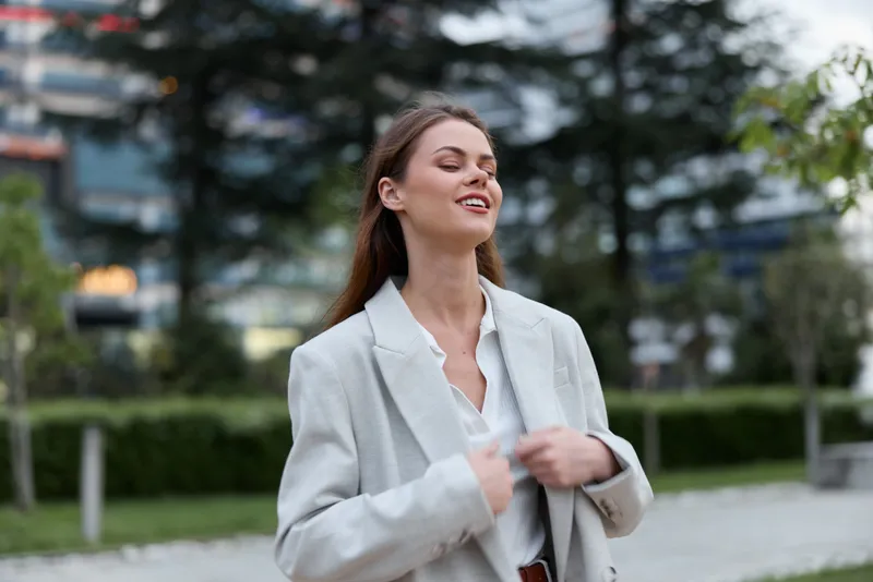 confident woman in light gray business suit smiling outdoors with urban background, natural makeup, professional style, spring season