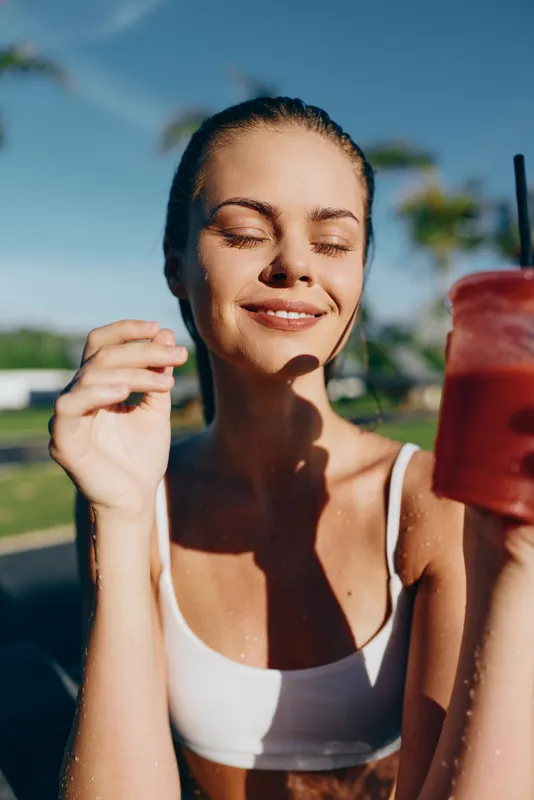 A smiling woman in athletic wear enjoys a bright outdoor setting, holding a smoothie. A lifestyle moment highlighting health, fresh air, and simple daily wellness.