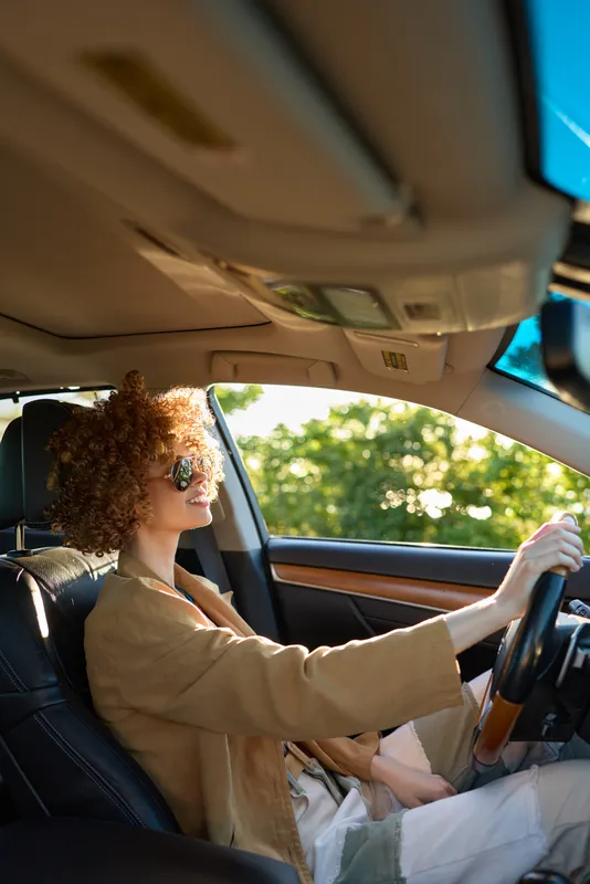 Cheerful woman driving a car, seated in a warm interior, sunny day, relaxed posture, retro film color vibe, natural light, candid lifestyle moment, motion, sunlit, colors