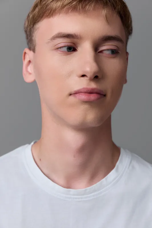 Young man face expression in a white t shirt under studio light, close up with neutral pose and calm mood, conveying clean aesthetic and minimal background