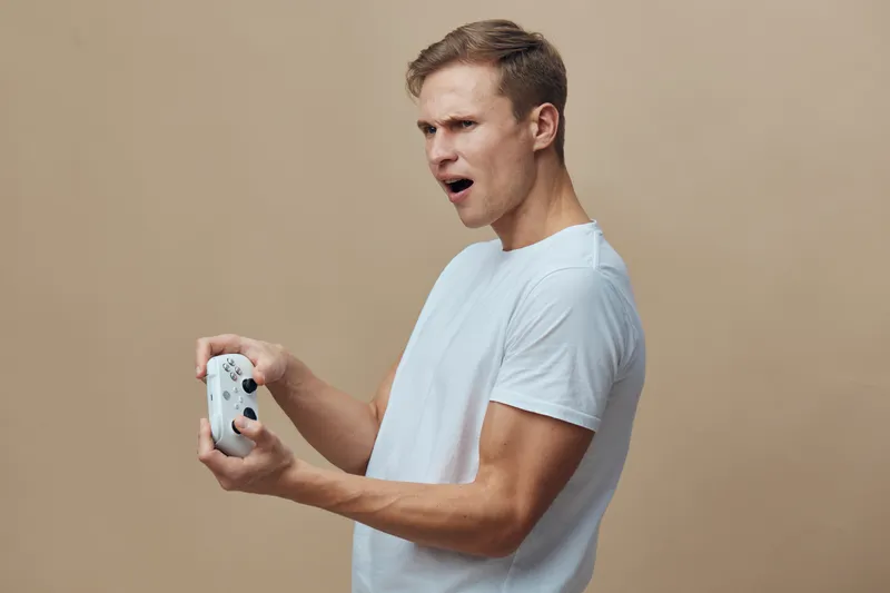 young man excited holding game controller play videogame casual wear white t-shirt beige background esports entertainment concept