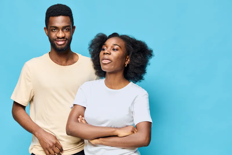 Happy young African couple smiling together against a light blue background, showcasing love and connection, with a stylish and modern appearance