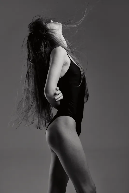 Black and white artistic portrait of a young woman in a black swimsuit with flowing hair and elegant pose.