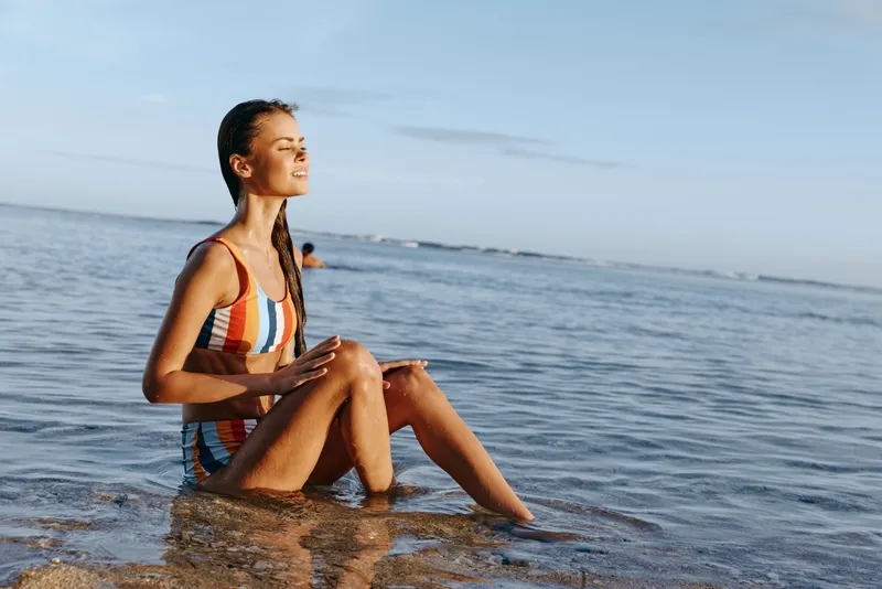 Woman yoga meditation by ocean seashore, balancing in seated pose on wet rock, soft sunrise colors, calm breathing, serene expression, gentle waves, quiet open coastal nature background