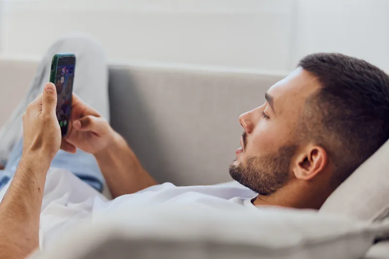 Relaxed man using smartphone while lounging on the couch, showcasing a modern lifestyle with vibrant colors and cozy atmosphere. Perfect for contemporary marketing needs.