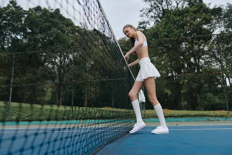 Young athletic woman in sports apparel poses confidently on a tennis court, showcasing determination and focus amidst a lush green background, perfect for fitness themes